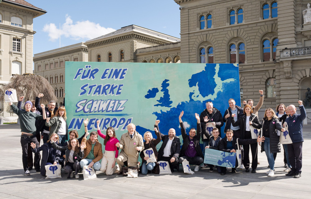 Die Europa-Allianz bestehend aus Vertreter:innen von Volt, Operation Libero, den Grünen, der Europäischen Bewegung Schweiz, VSS und weiteren vor einer Leinwand auf dem Bundesplatz. Die Leinwand zeigt eine Karte Europas, mit der fehlenden Schweiz in der Mitte. Links steht die Aufschrift: 