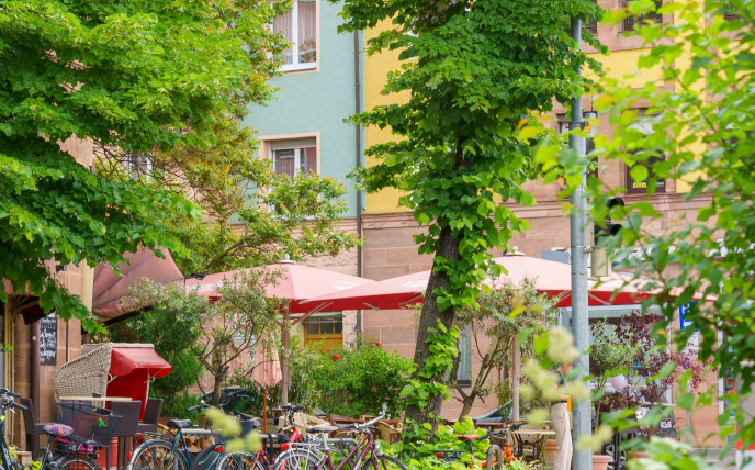 Café im Freien mit nahegelegenen geparkten Fahrrädern und bunten Gebäuden, umgeben von Bäumen und üppigem Grün