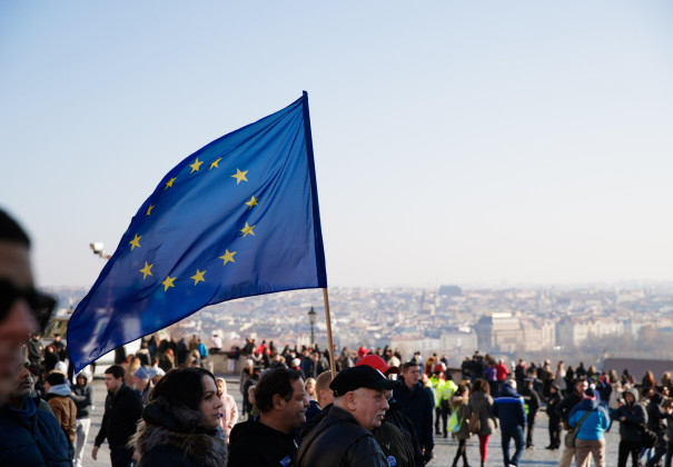 Bild einer Demonstration. Im Fokus steht eine EU Flagge, die im Wind weht