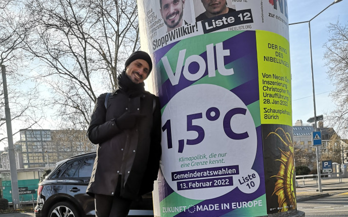 ZH Gemeinderatskandidat Danilo Lo Pumo, der an einer Säule mit einem Wahlplakat von Volt Schweiz steht.